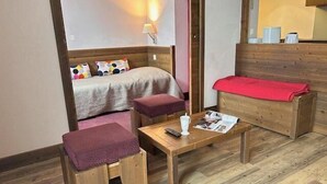 Ein gemütliches Zimmer mit einem Bett, einem kleinen Tisch mit Fernbedienung, einer Zeitschrift und einer roten Decke auf einer Bank.