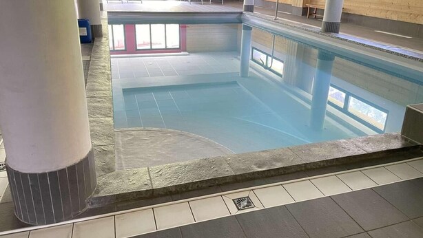 Ein Hallenbad mit klarem Wasser, gefliesten Wänden und einigen Liegestühlen.