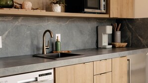 Een moderne keuken met houten kastjes, een RVS vaatwasser, een zwarte magnetron en een marmeren aanrechtblad.