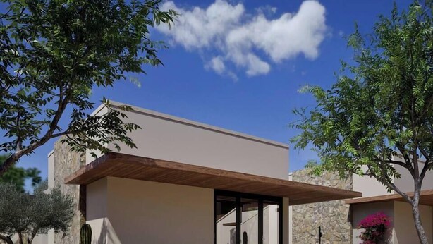 Een modern huis met een overdekte patio, een stenen muur en diverse woestijnplanten.