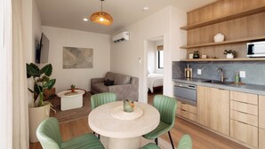 Een moderne keuken met houten kastjes, een ingebouwde magnetron en een spoelbak. Er is een eethoek met een ronde tafel en groene stoelen.