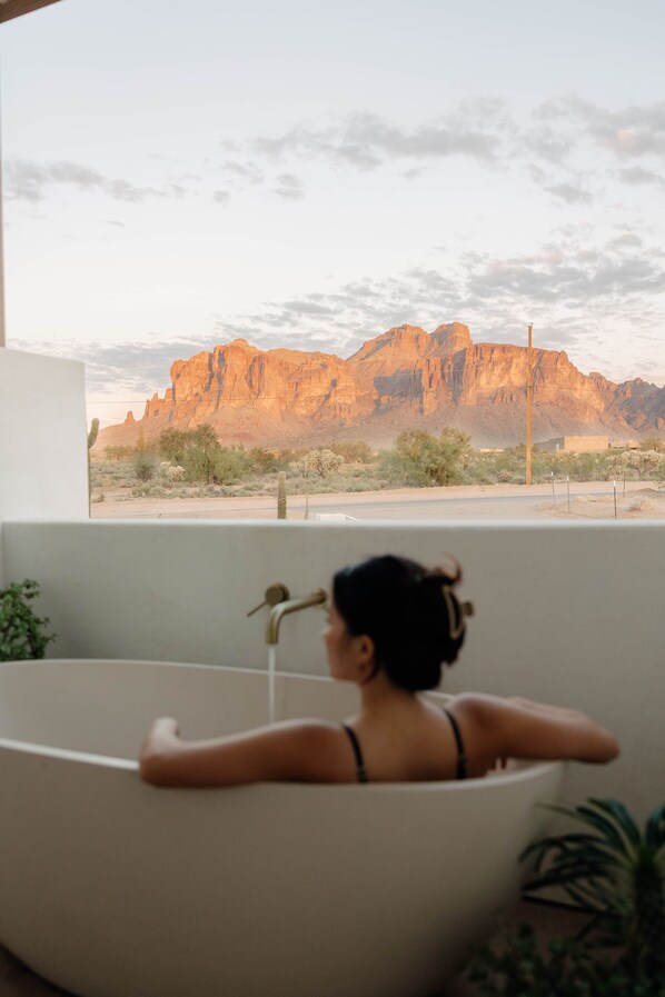 A woman in a bathtub with a view of a desert landscape and mountains.