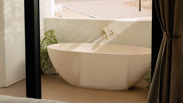 A bedroom with a large bathtub, a bed, and a view of a mountainous landscape through a window.