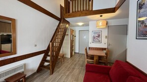 Escada leva a um quarto no mezanino, área de jantar com mesa e cadeiras, e um sofá vermelho em uma sala de estar.