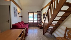 Una habitación acogedora con sofá rojo, mesa de madera y escalera.