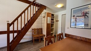 Una habitación con escalera de madera, una mesa de comedor, sillas, un banco de madera y estanterías empotradas.