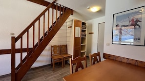 A room with a wooden staircase, a dining table, chairs, a wooden bench, and a built-in shelving unit.
