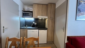 A compact kitchen with wooden cabinets, a microwave, a coffee maker, and a dishwasher.