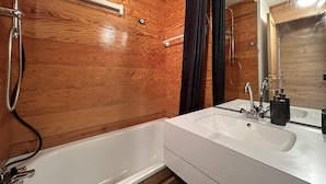 Un bagno con parete in legno, una vasca da bagno bianca e un lavabo con specchio sopra.