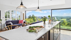 A modern kitchen with a large island, a dining area with a sofa, and a view of the countryside. - Fox Hill House in Haytor (Newton Abbot)
