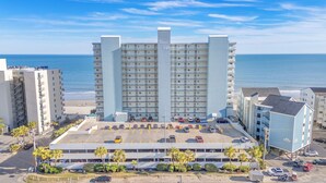 Un hotel a più piani con un parcheggio di fronte, situato vicino alla spiaggia.