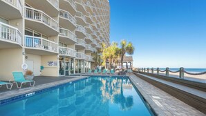 Una piscina con lettini, vista sulla spiaggia e un edificio con balconi.