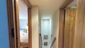 Een smalle houten gang met een bed aan het einde, houten deuren en een trap.