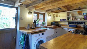 Een landelijke keuken met houten balken, een wasmachine en planken met keukengerei.