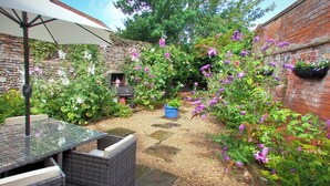 Een terras met rieten meubilair, een barbecue en diverse bloeiende planten.