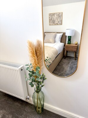 A bedroom with a bed, bedside table, lamp, and a mirror reflecting the room.