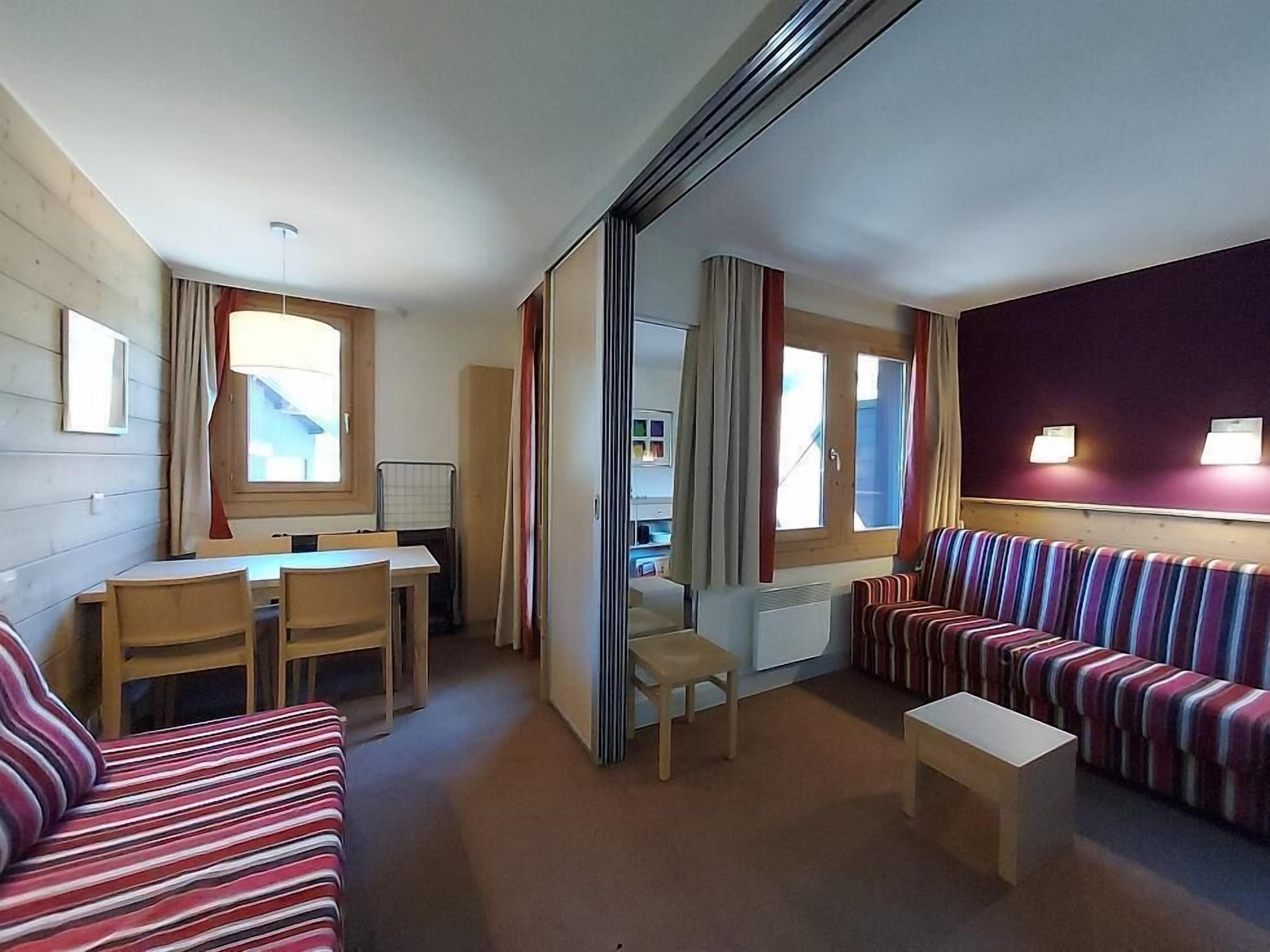 A compact hotel room with a dining area, a sofa, a small table, and a mirror.