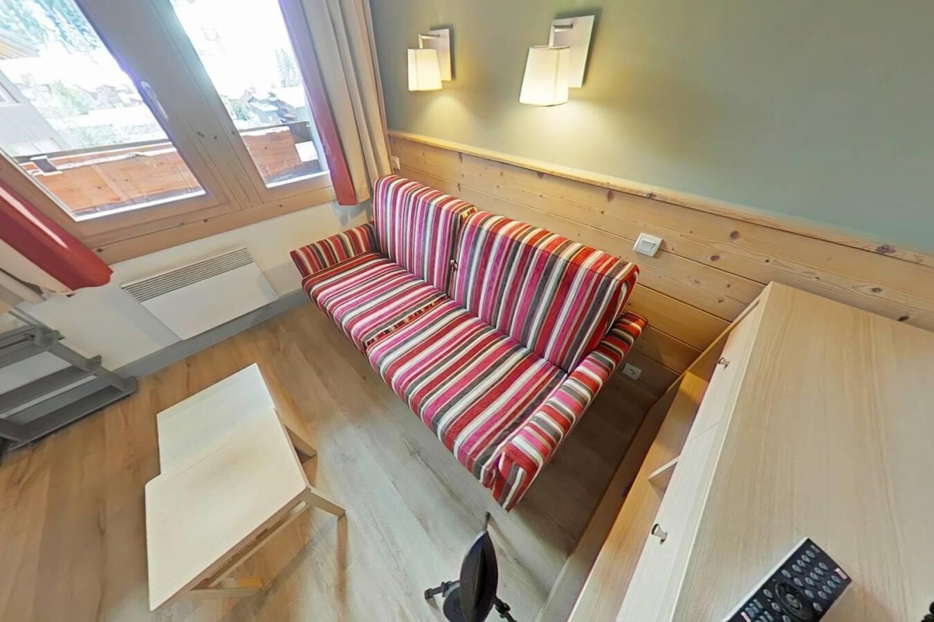 Una habitación con un sofá a rayas, paredes de madera y una ventana con cortinas.