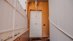 Un escalier étroit mène à une porte blanche surmontée d’une lanterne décorative.