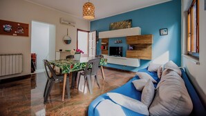 Un salon moderne avec un canapé bleu, une table à manger avec des chaises, un luminaire suspendu et une cheminée.