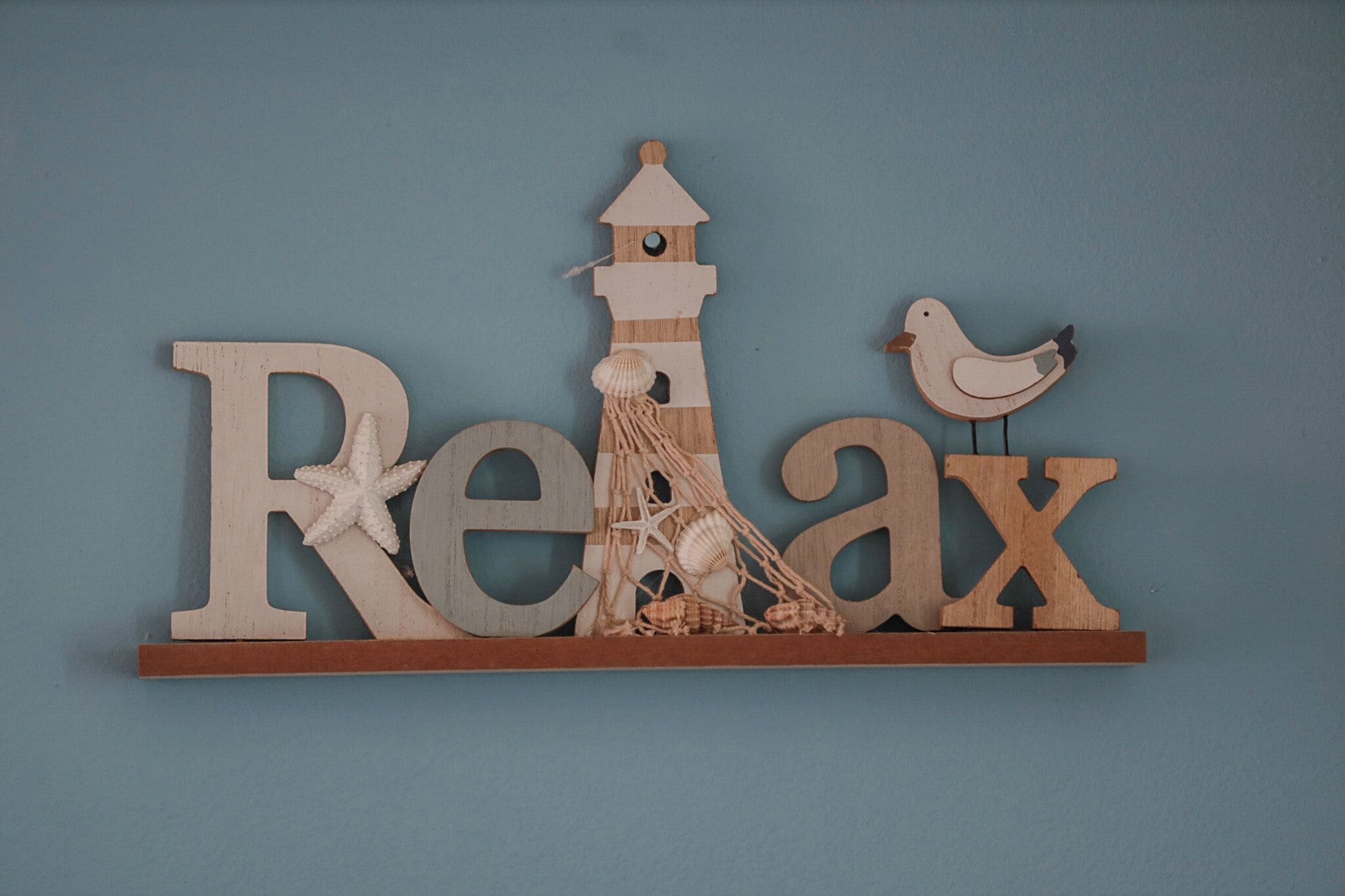 A wooden sign with the word "Relax" and a lighthouse, starfish, and a bird.