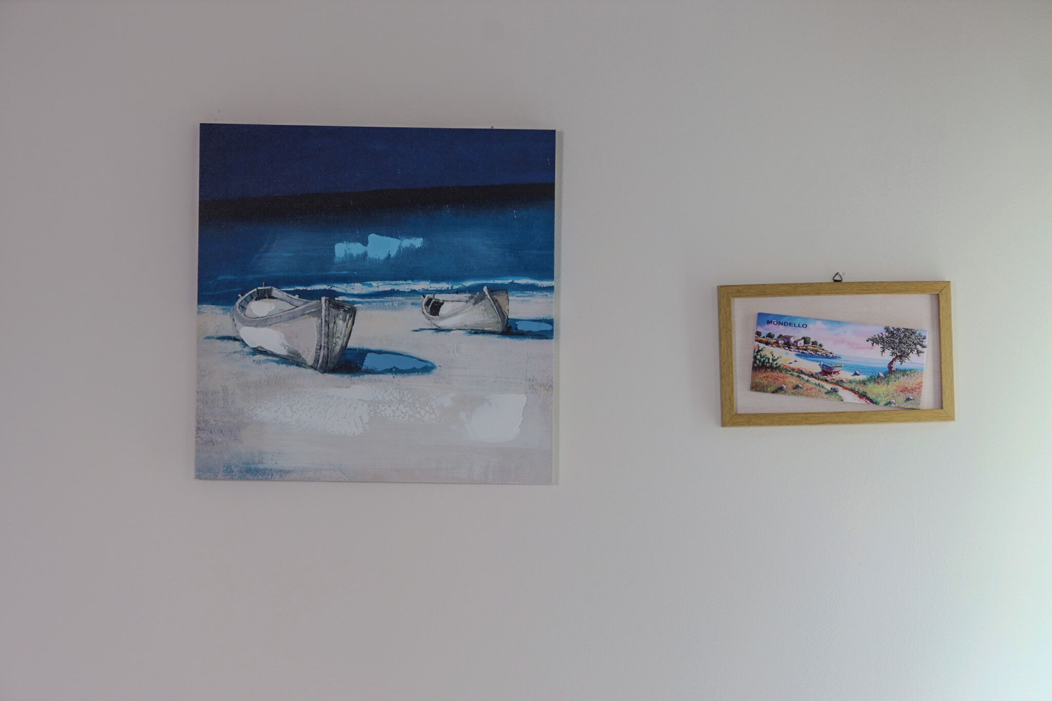 A painting of boats on a beach and a framed picture on the wall.