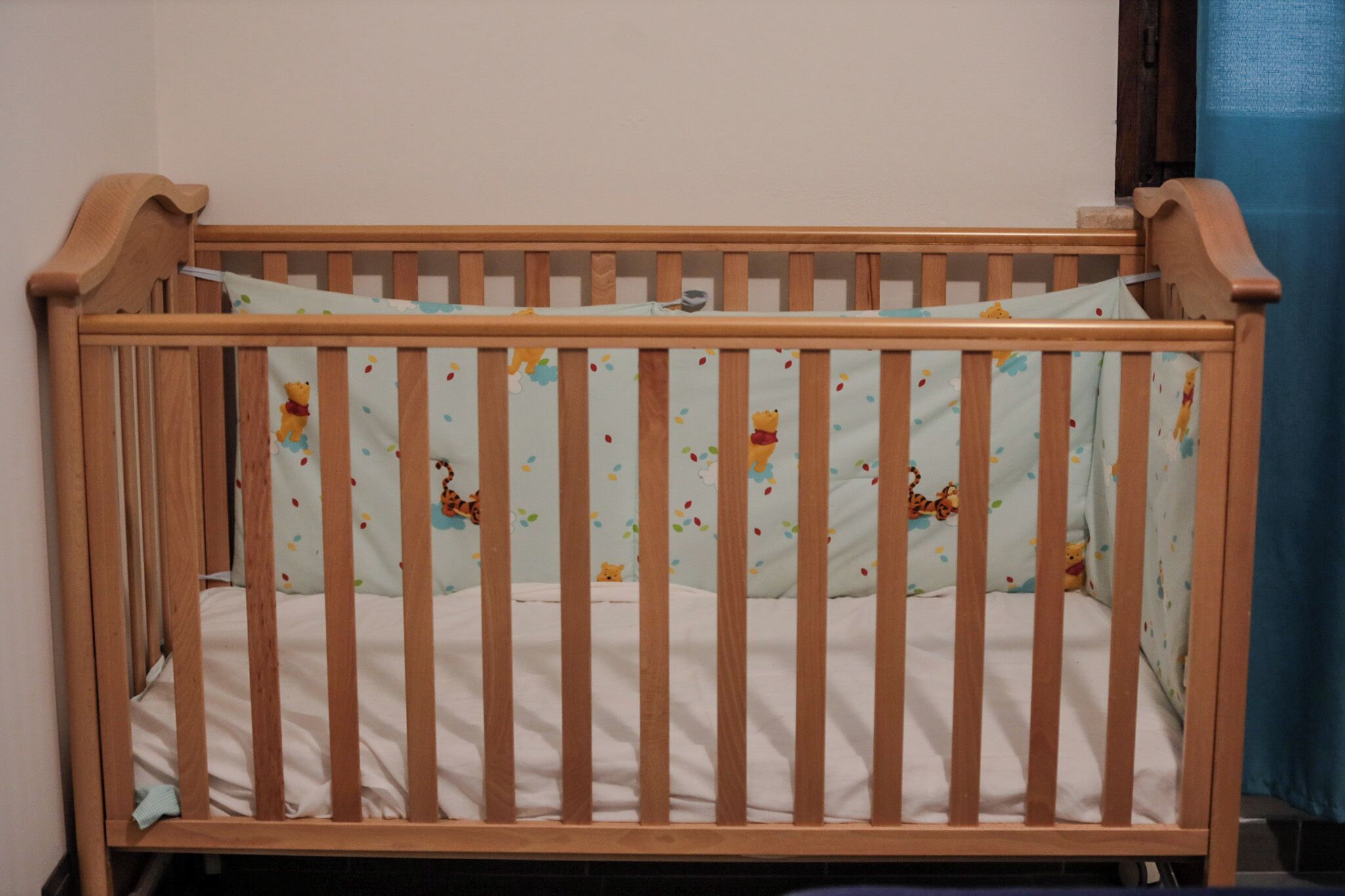 A wooden crib with a white mattress and a light blue crib sheet with animal prints.
