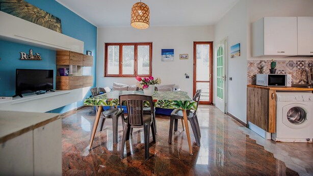 Une cuisine moderne équipée d’un lave-linge, d’un coin repas avec une table et des chaises, et d’un téléviseur posé sur une étagère.