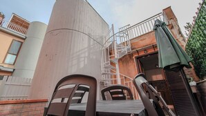 Un bâtiment doté d’un escalier en colimaçon menant à un balcon, d’un grand réservoir cylindrique et d’un parasol vert.