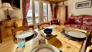 A cozy dining area with a wooden table set for two, a red patterned sofa, and a view of the outdoors through large windows. - 4th floor, balcony, tv, 28m², Serre Chevalier (La Salle-les-Alpes)