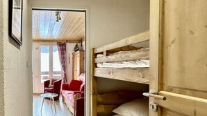 A narrow hallway with a wooden door leading to a room with bunk beds and a red sofa. - 4th floor, balcony, tv, 28m², Serre Chevalier (La Salle-les-Alpes)