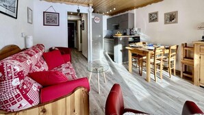 A cozy living room with a red sofa and wooden furniture, a dining area with a table and chairs, and a kitchen in the background. - 4th floor, balcony, tv, 28m², Serre Chevalier (La Salle-les-Alpes)