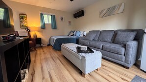 A living room with a grey sofa, a wooden floor, a ceiling fan, and a TV mounted on the wall. - Charming tiny home only 15 mins from Town of Warrenton & Town of Culpeper (Rixeyville)