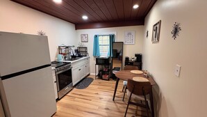 A compact kitchen with a refrigerator, stove, and sink, wooden flooring, and a dining area with two chairs and a table. - Charming tiny home only 15 mins from Town of Warrenton & Town of Culpeper (Rixeyville)