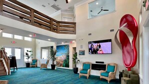Un vestíbulo amplio con techo alto, una gran pantalla de televisión, muebles de mimbre y un mural tropical.