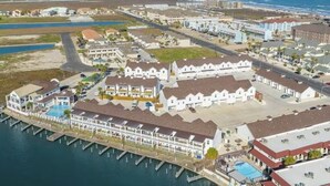 Vista aérea de un hotel costero con varias construcciones, un puerto deportivo y una playa al fondo.