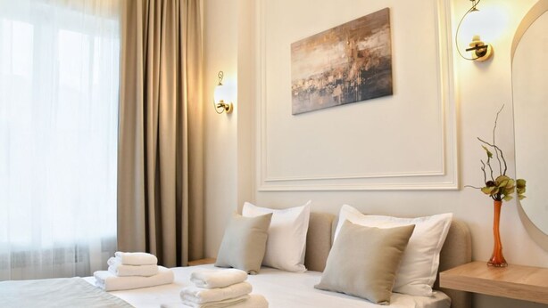 Ein Hotelzimmer mit einem Bett, Kissen, einem Nachttisch, einer Vase mit Blumen und einem Bild an der Wand.