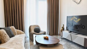 Ein modernes Wohnzimmer mit einer Couch, einem Sessel, einem Couchtisch und einem Flachbildfernseher, der "DiAngelo Guest House" zeigt.