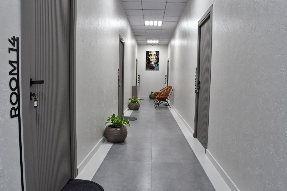 A hallway with doors labeled 'ROOM 14' and 'ROOM 15', potted plants, and a chair.