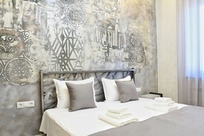 Una camera d'albergo con un letto, cuscini e una parete decorata con un murale raffigurante un panorama urbano.