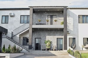 A modern two-story building with a concrete facade, a staircase leading to the entrance, and outdoor seating with potted plants. - DiAngelo Guesthouse|Studio 15 (Yerevan)