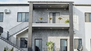 A modern two-story building with a balcony, a staircase, and a large planter with flowers.