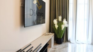A modern hotel lobby with a mounted television displaying the hotel's name, a minimalist console table, and a potted plant.