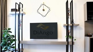 A modern interior with a mounted TV displaying the DiAngo logo, a minimalist plant, and a geometric wall decoration. - DiAngelo Guesthouse|Studio 13 (Yerevan)