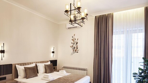 A modern hotel room with a large bed, a radiator, a chandelier, and a potted plant. - DiAngelo Guesthouse|Studio 13 (Yerevan)