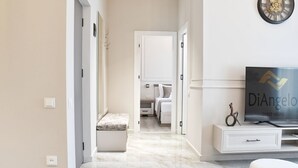 Una habitación de hotel moderna con piso de mármol, una cama, un televisor sobre un mueble blanco y un reloj en la pared.