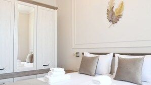 Una habitación de hotel con un espejo grande, una cama con ropa blanca y una hoja decorativa en la pared.