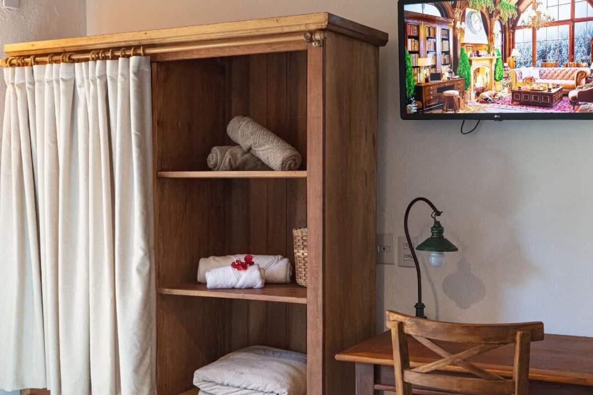 Une pièce comprenant une armoire en bois, un téléviseur fixé au mur, une petite table et une lampe.