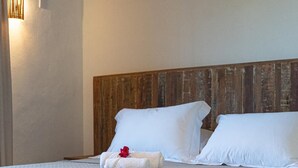 Un lit bien fait, avec du linge de lit blanc et des oreillers, une tête de lit en bois et une petite serviette ornée d’une fleur rouge sur le côté.