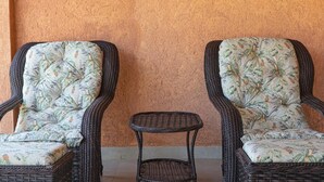 Deux fauteuils en osier ornés de coussins à motifs floraux et une petite table en osier, le tout placé devant un mur à texture.